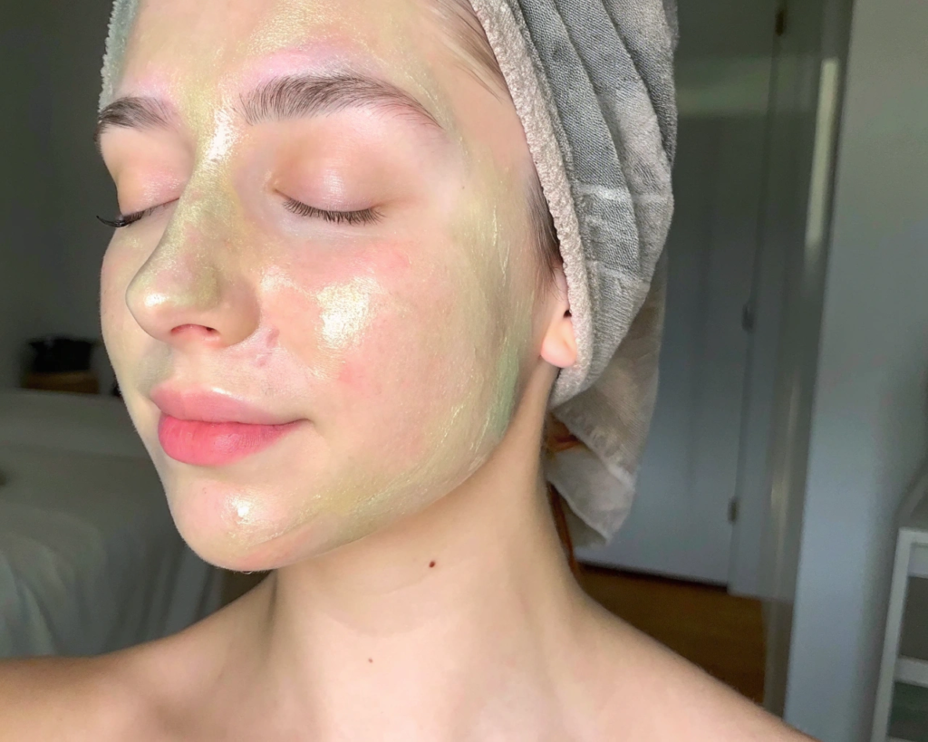 A serene close-up view of a woman's face, gently applying a natural, homemade facial mask. The mask's vibrant, earthy hues blend seamlessly with her glowing skin, radiating a sense of rejuvenation and self-care. Soft, diffused lighting casts a warm, soothing glow, highlighting the mask's natural ingredients and the model's tranquil expression. In the background, a blurred, minimalist setting evokes a spa-like ambiance, emphasizing the calming and nourishing experience of using natural facial masks. The overall composition conveys the beneficial effects of these homemade treatments, inviting the viewer to embrace the simplicity and efficacy of natural skin care. Como Fazer uma Máscara Facial com 3 Ingredientes